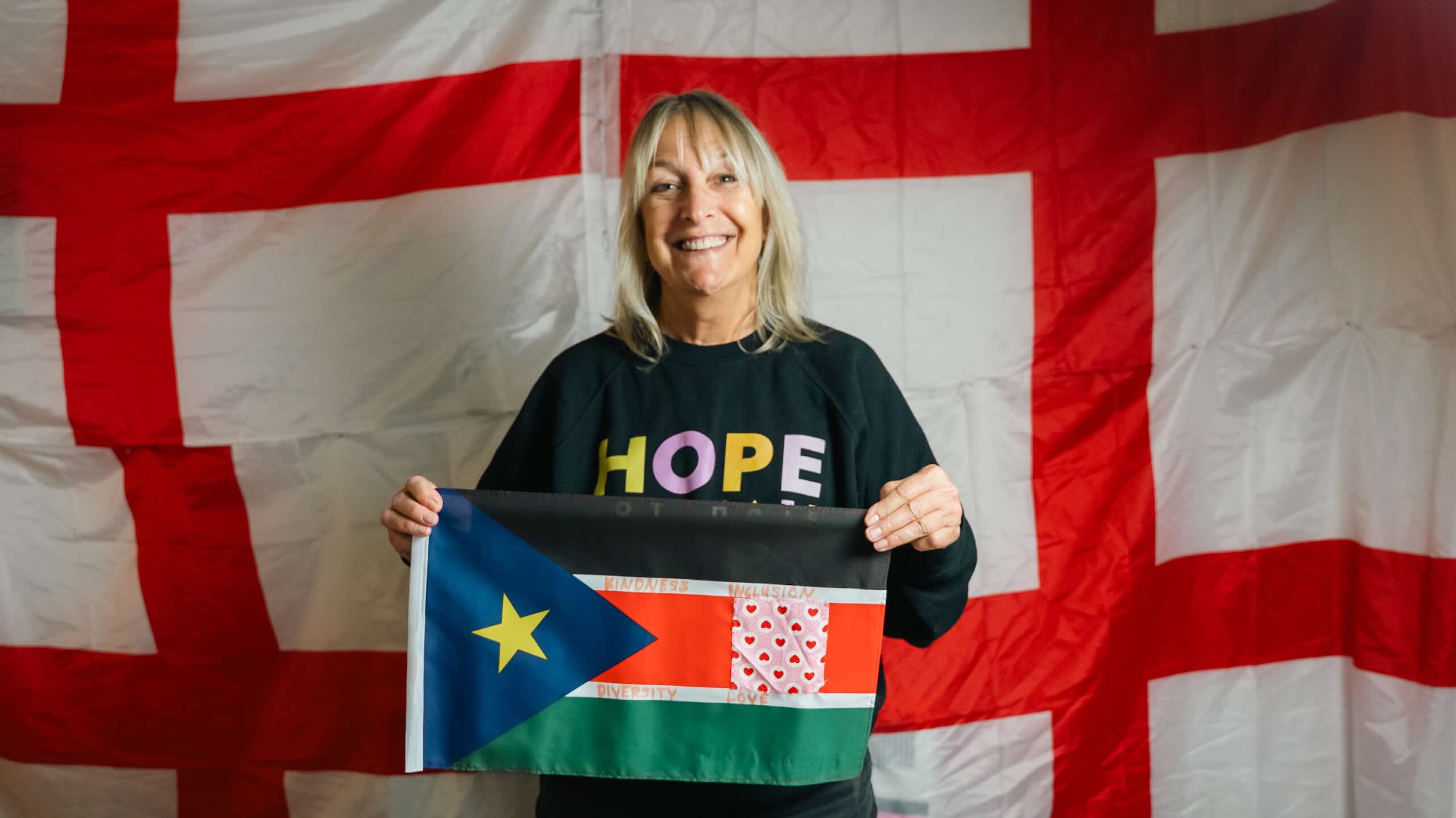 A smiling person holds a beige textile panel decorated with folded red, blue and white flag fabric and small embroidered yellow stars.