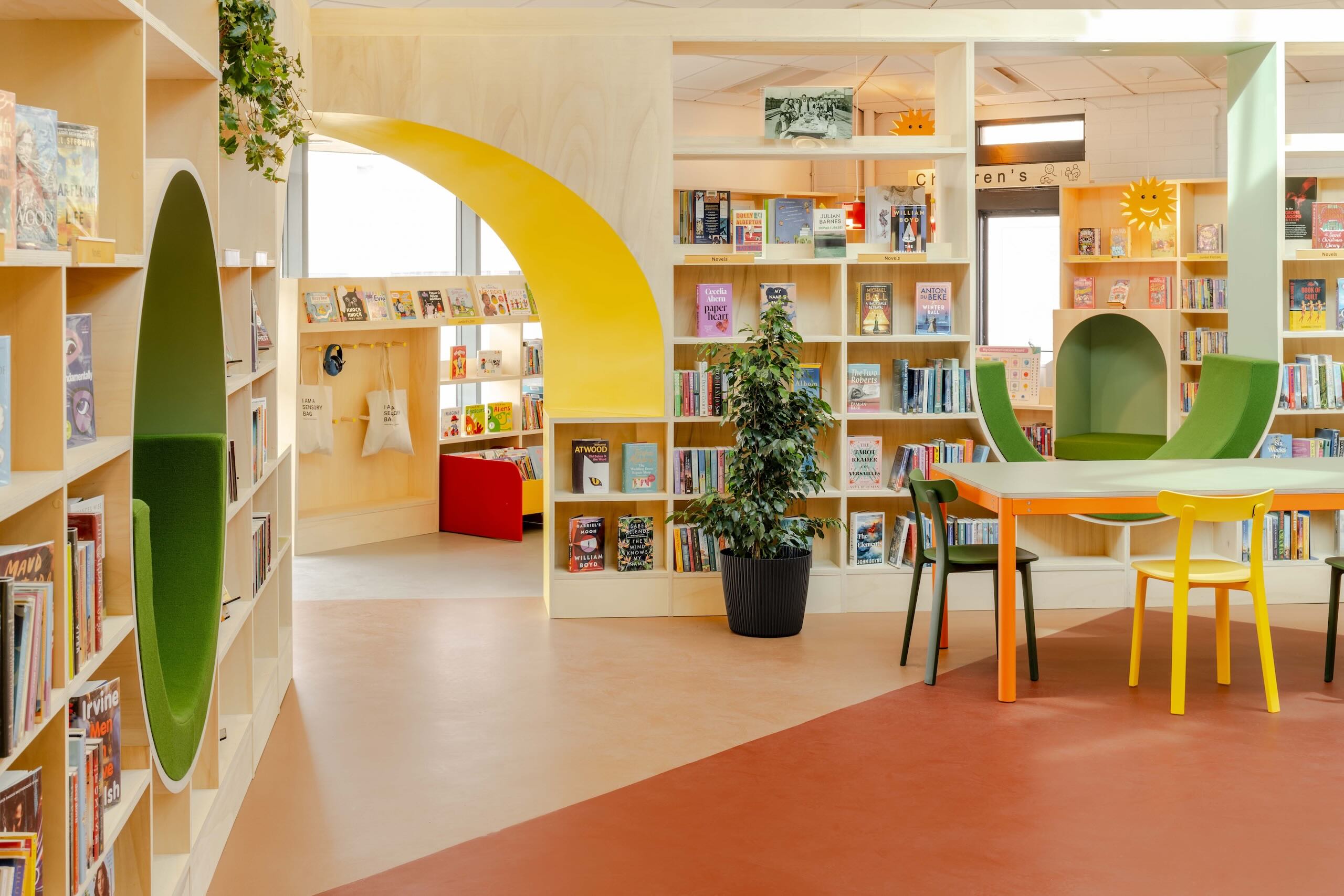 Interior view of Haydock Library with a large yellow arch, bookshelves, seating nooks and study table linking different library zones.