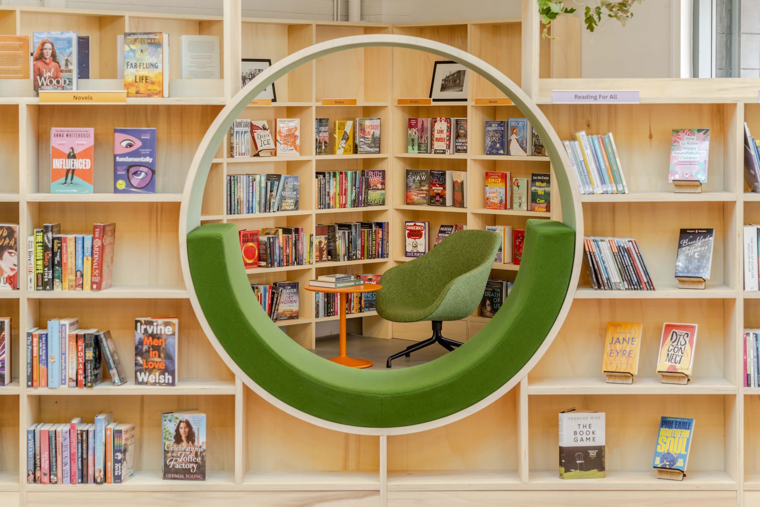 Close-up of circular green reading nook containing an upholstered chair and side table, surrounded by library shelving.