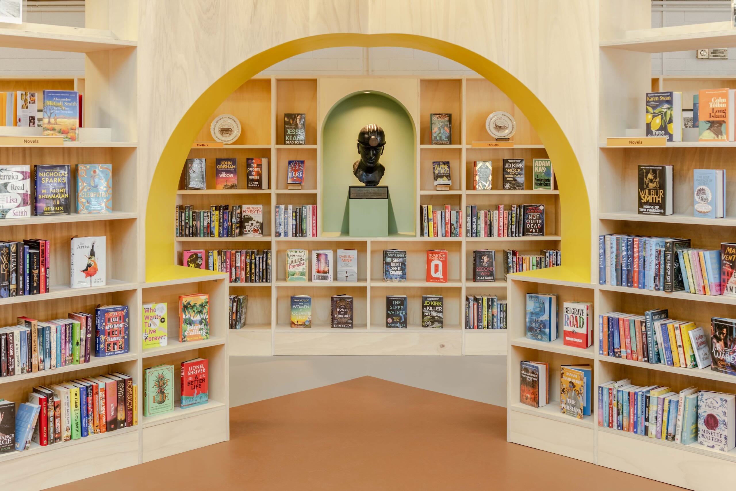 View through a yellow arch framing shelving and a bust titled The Minor by sculptor Elizabeth Frink, displayed in a display nook.