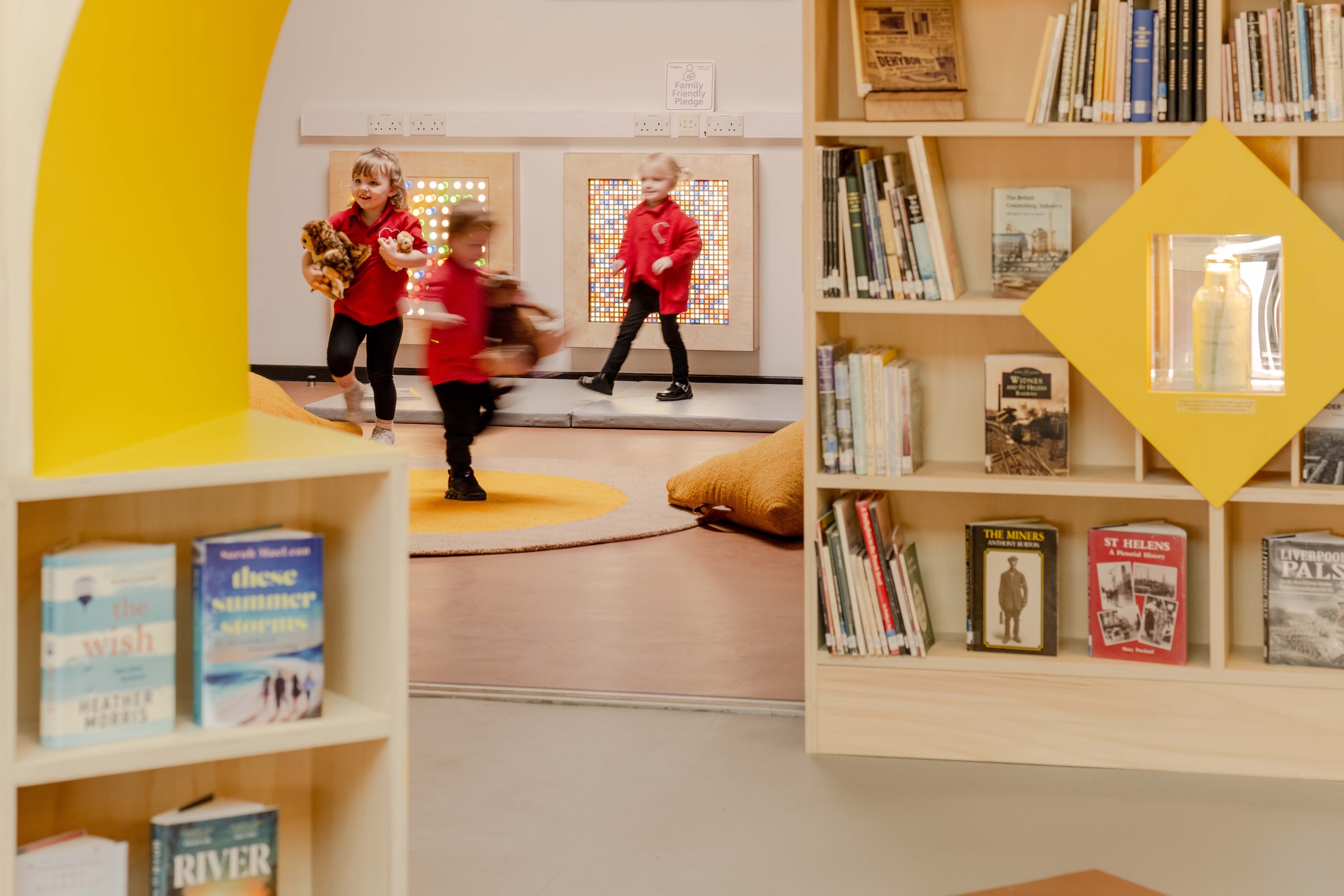 Three children wearing red school jumpers playing in a sensory room, which has sensory panels in the background.