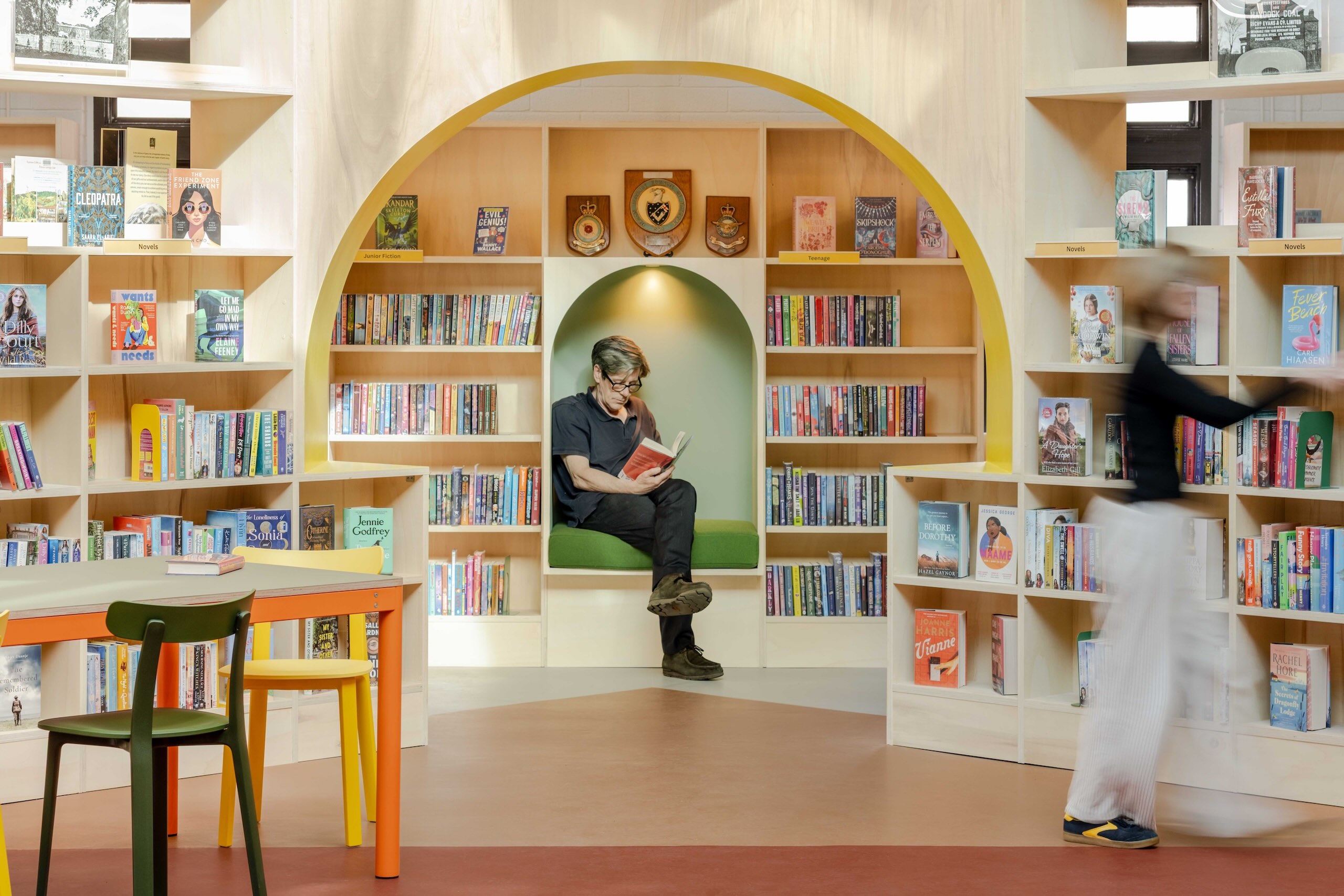 A large arch frames a green reading nook with a man sat inside reading a book.