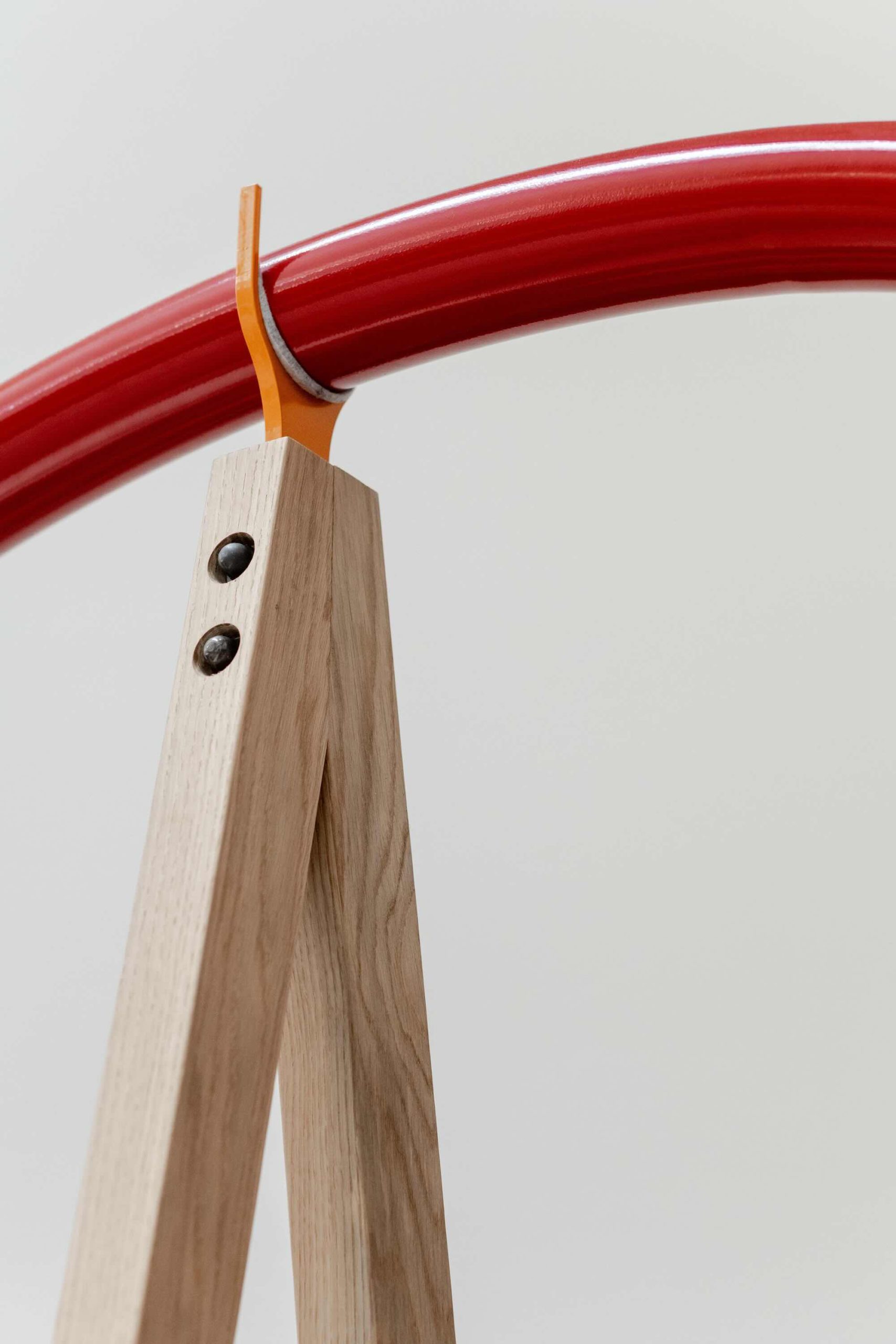 Listening Desk by Emily Peasgood is a mid-century-inspired desk with a very large red metallic horn joined to it. It emerges out the back and round all the way over the desk, finishing above the listener's head. From the side, it looks like a huge base clef or ear. It looks like something from Dr Seuss. Sound can only be heard from under the horn. There is bespoke software on the screen that allows members of the public to listen to archival sound recordings and remix them. This is a close-up of the tuning fork that the horn sits upon to hold it securely in place.