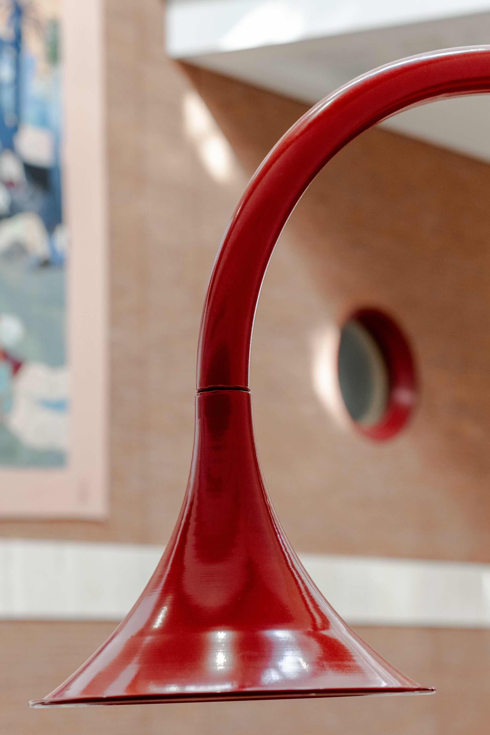 Listening Desk by Emily Peasgood is a mid-century-inspired desk with a very large red metallic horn joined to it. It emerges out the back and round all the way over the desk, finishing above the listener's head. From the side, it looks like a huge base clef or ear. It looks like something from Dr Seuss. Sound can only be heard from under the horn. There is bespoke software on the screen that allows members of the public to listen to archival sound recordings and remix them. This is a side profile of the horn bell that sits above a listener's head.