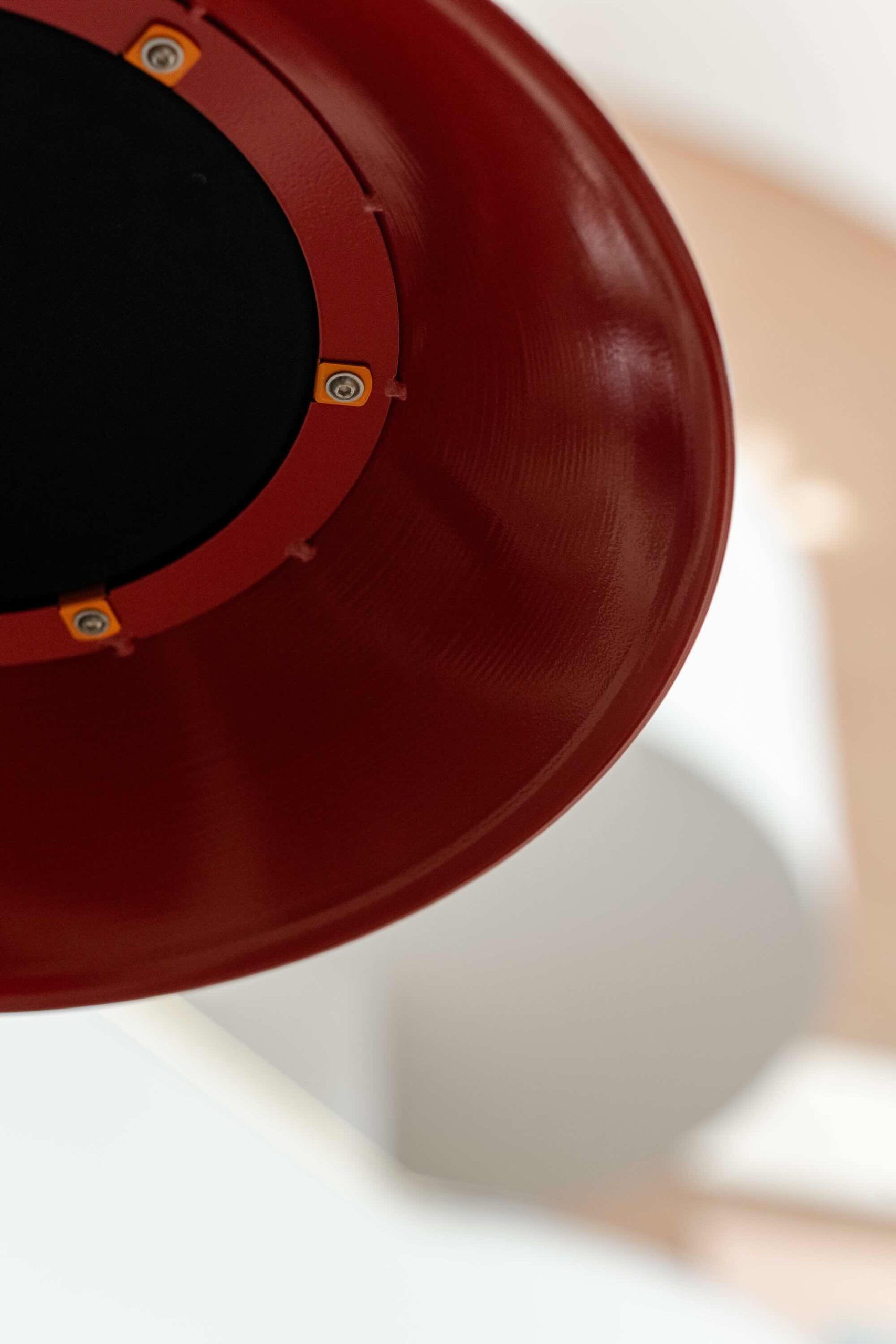 Listening Desk by Emily Peasgood is a mid-century-inspired desk with a very large red metallic horn joined to it. It emerges out the back and round all the way over the desk, finishing above the listener's head. From the side, it looks like a huge base clef or ear. It looks like something from Dr Seuss. Sound can only be heard from under the horn. There is bespoke software on the screen that allows members of the public to listen to archival sound recordings and remix them. This is a close up of the horn, showing the speaker attached underneath it.