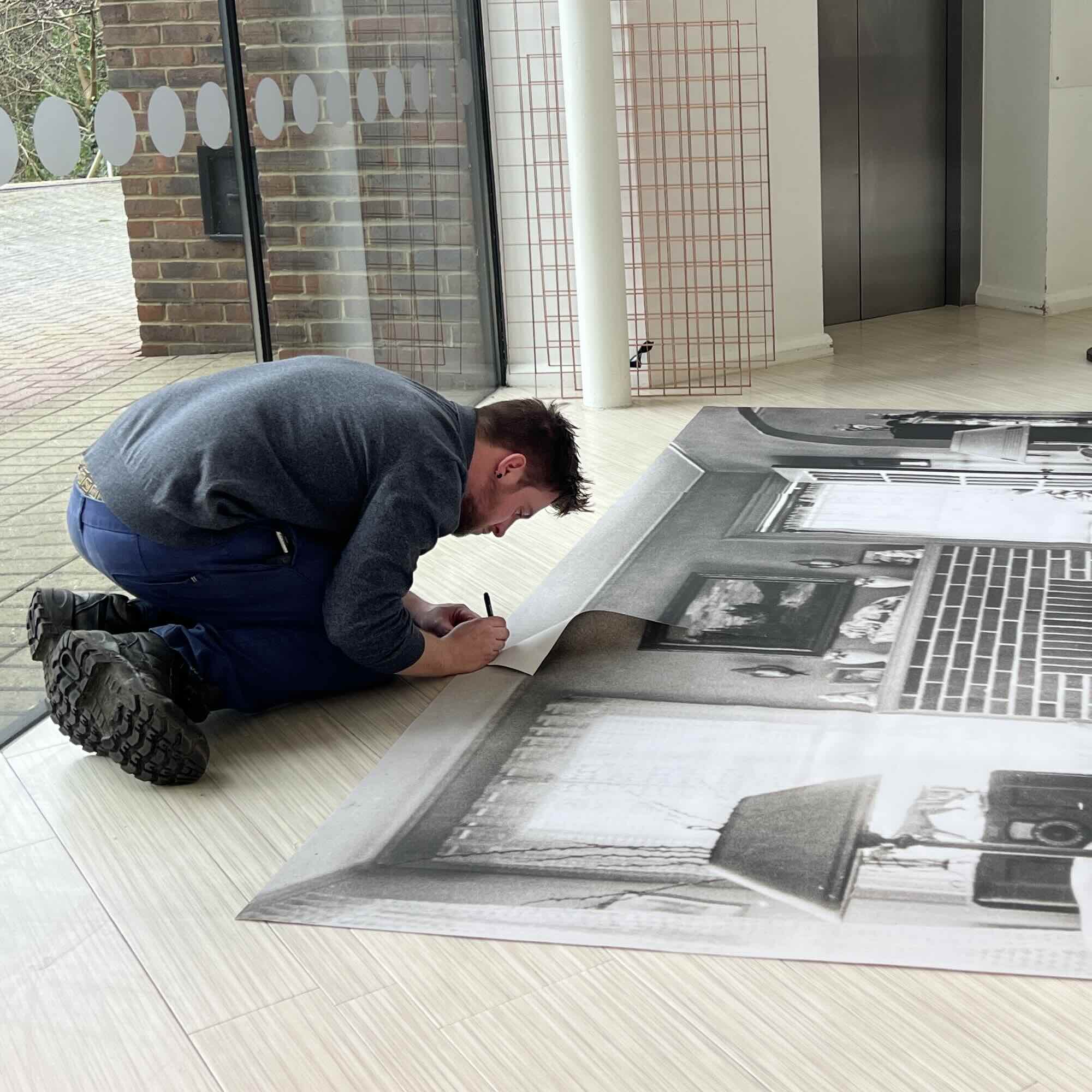 Ben Jason This is a picture of Ben Jason who helped to install the artwork and create the audio player. In this picture, Ben is working on the ground, connecting the backdrop panels together. Backdrop panels were placed behind the Threaded Shelter to make it look like a WWII living room scene.