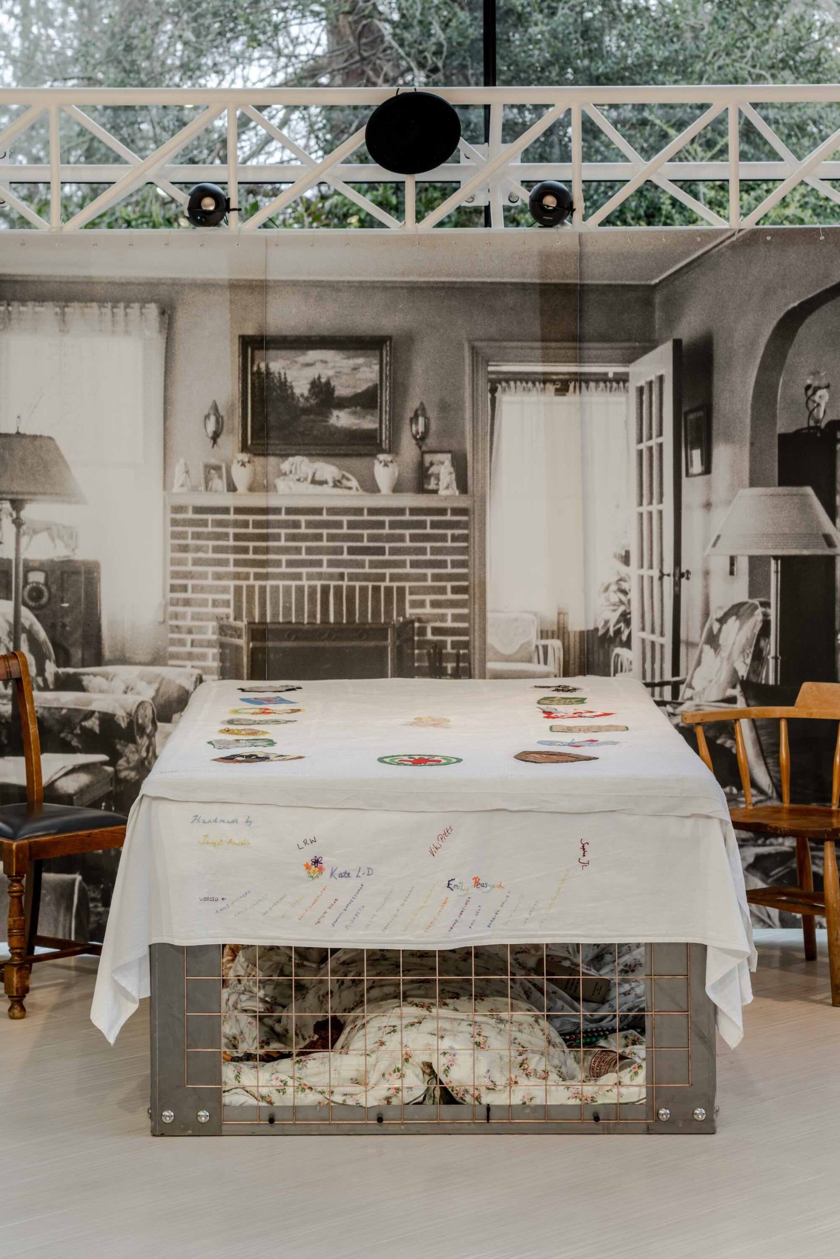 This is a photo of Threaded Shelter by Emily Peasgood. It is a recreation of a Morrison Shelter from WW3 with a bespoke tablecloth containing clothing repair patches. When you touch each patch, a voice tells a story.