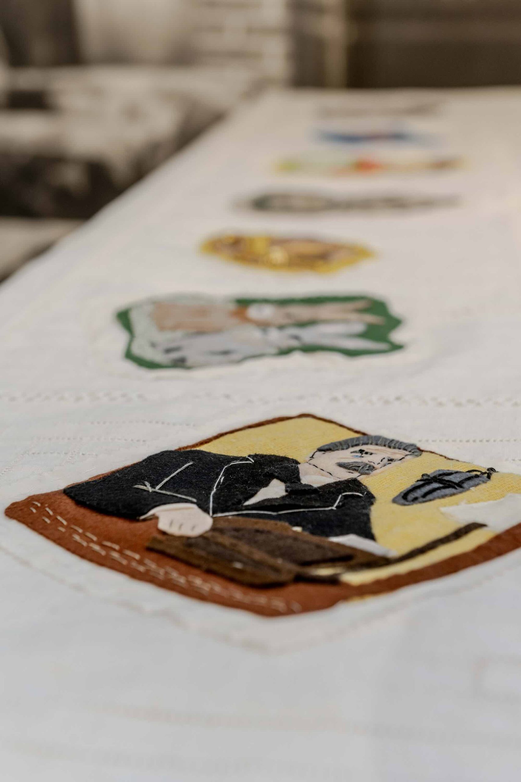This is a photo of Threaded Shelter by Emily Peasgood. It is a recreation of a Morrison Shelter from WW3 with a bespoke tablecloth containing clothing repair patches. When you touch each patch, a voice tells a story. This photo focuses on a patch of Neville Chamberlain.